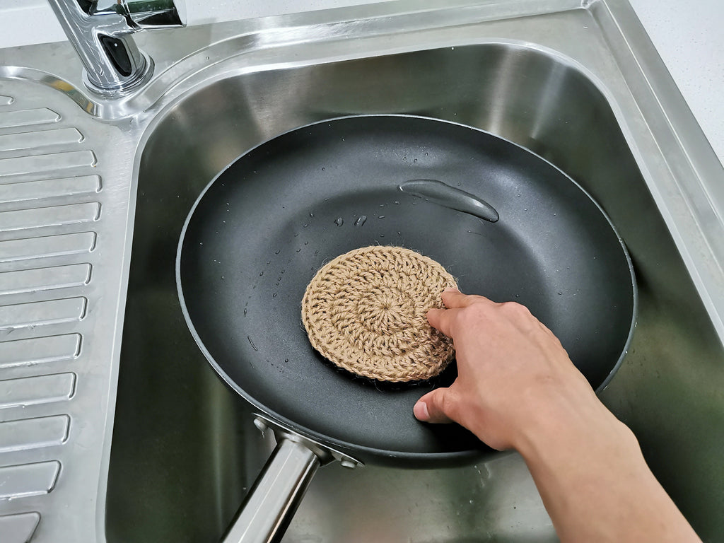 Washing a frying pan with a jute scrubber