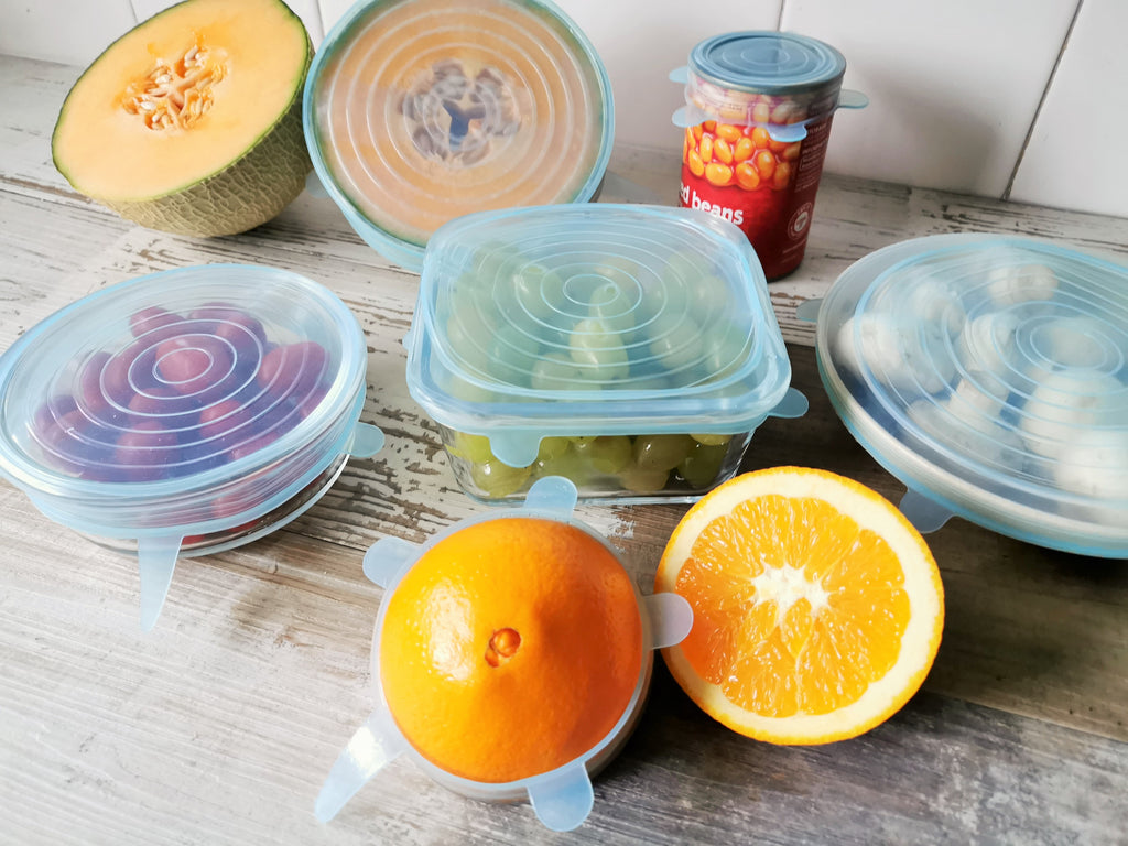 Silicone stretch lids light blue are covering round container, square container, oval plates, canned food, half cut orange and melon.