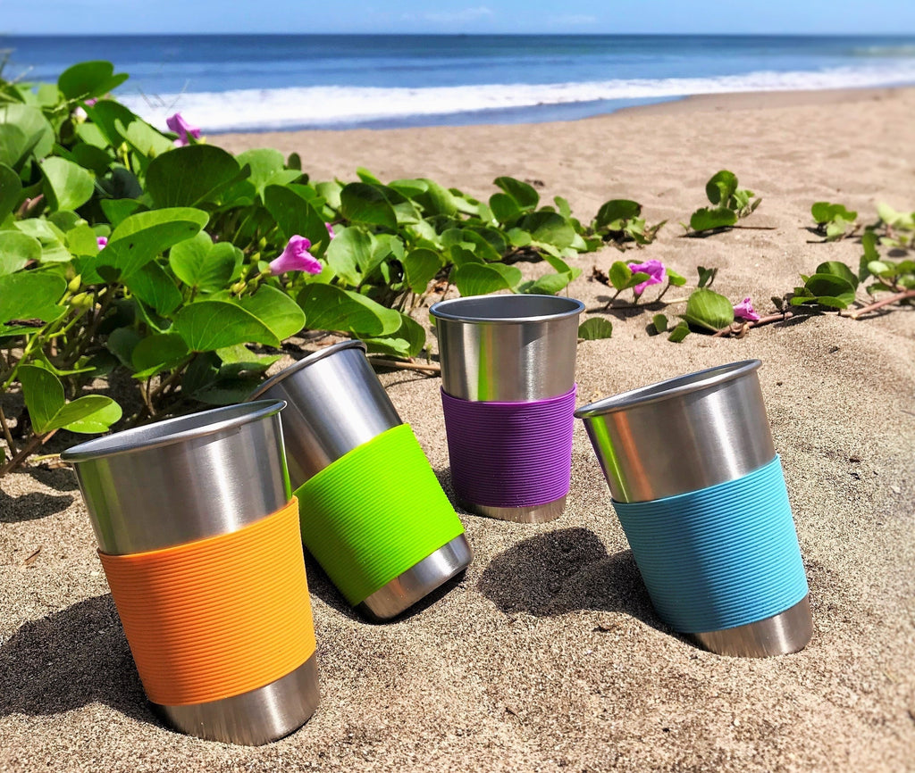 Stainless steel cups orange, green, purple and blue at the beach